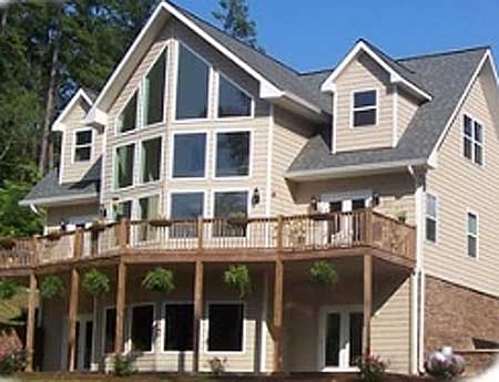 House plan exterior: Modern style, two-story home with a large multi-pane window wall, wraparound deck, and gabled dormers.