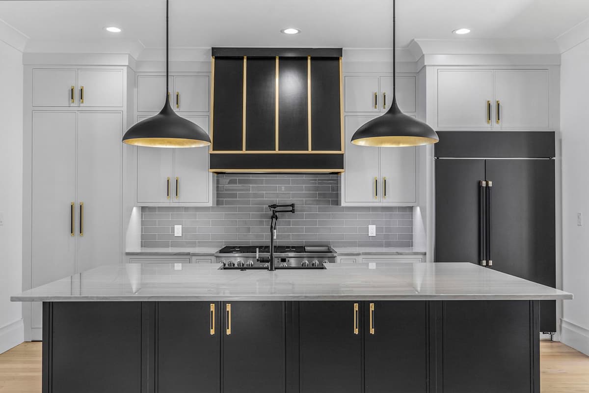 Modern kitchen with a large island, grey subway tile backsplash, gas range, and black and gold range hood.