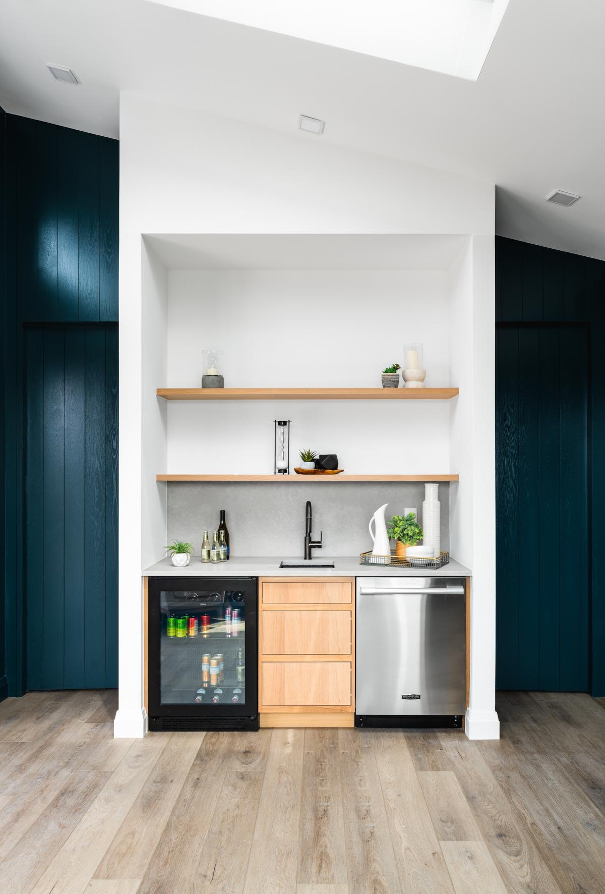 Wet bar with beverage fridge, sink, dishwasher, and wood cabinetry against a textured teal wall.