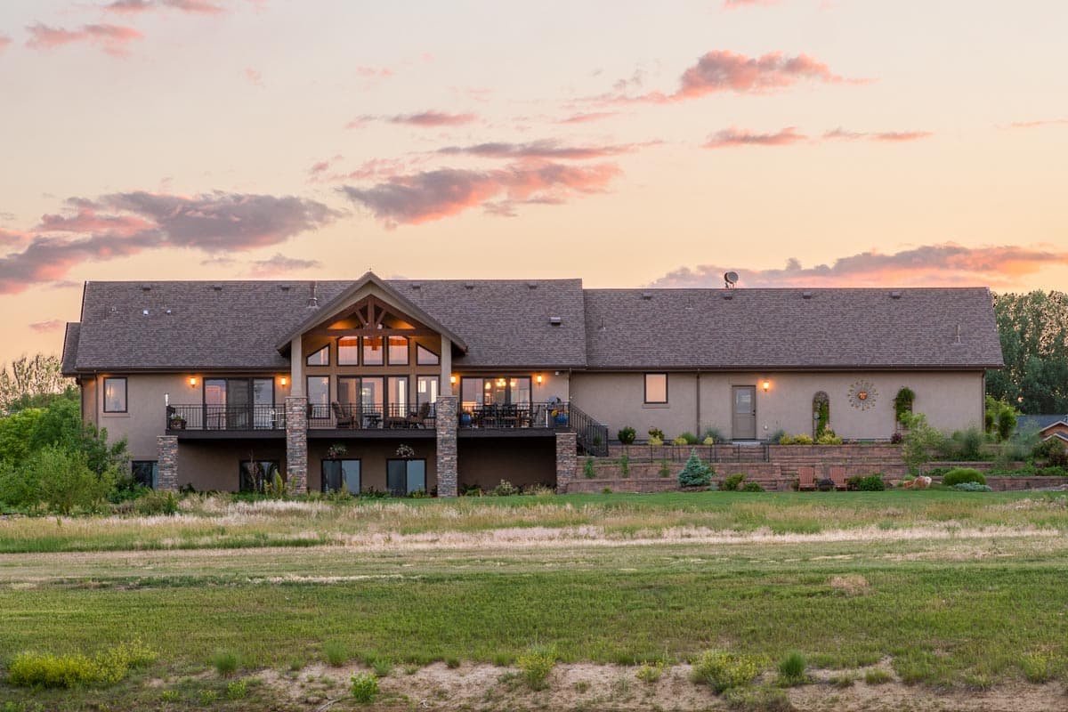 House plan exterior: Long ranch home with large central gabled window section, covered balcony, and stone accents.