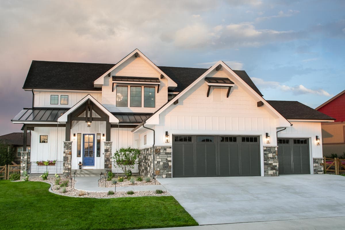 House plan exterior. Two-story Modern Farmhouse with gabled roof, covered porch with stone columns, and three-car garage.