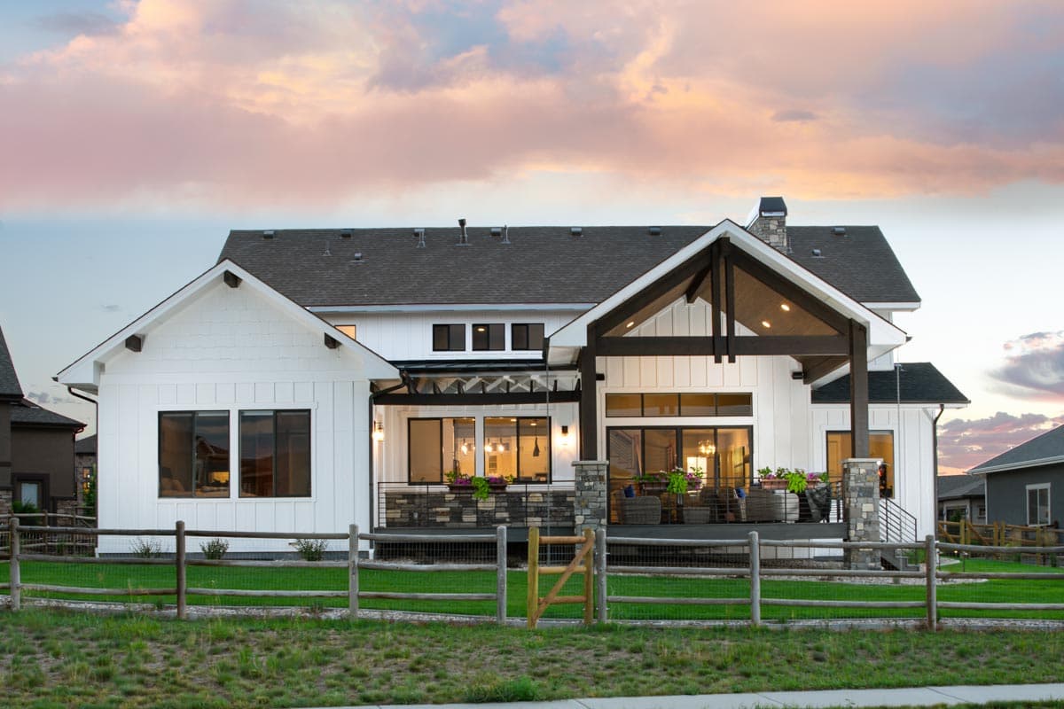 Modern Farmhouse house plan exterior with white board and batten siding, gables, covered patio, and stone chimney.