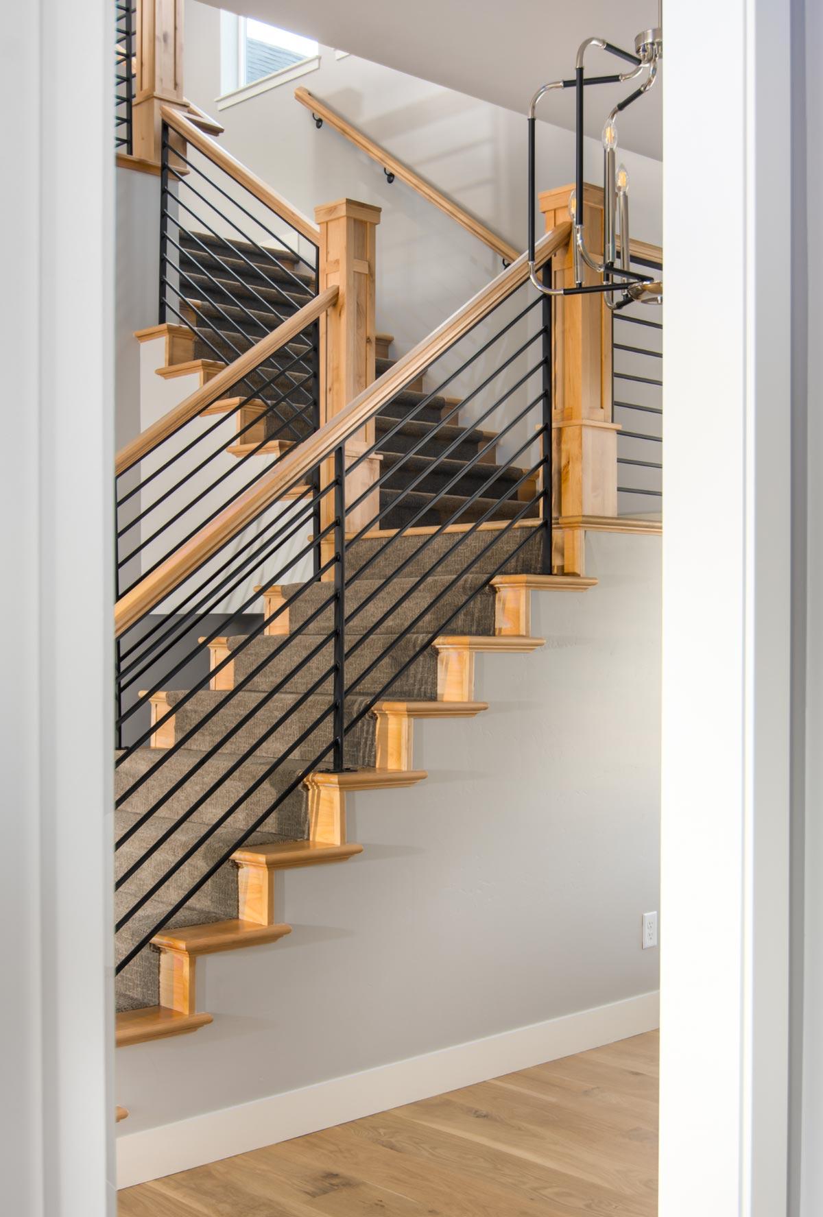 Interior staircase with wood treads, carpet runner, and black metal railing. Features wood newel posts and contemporary chandelier.