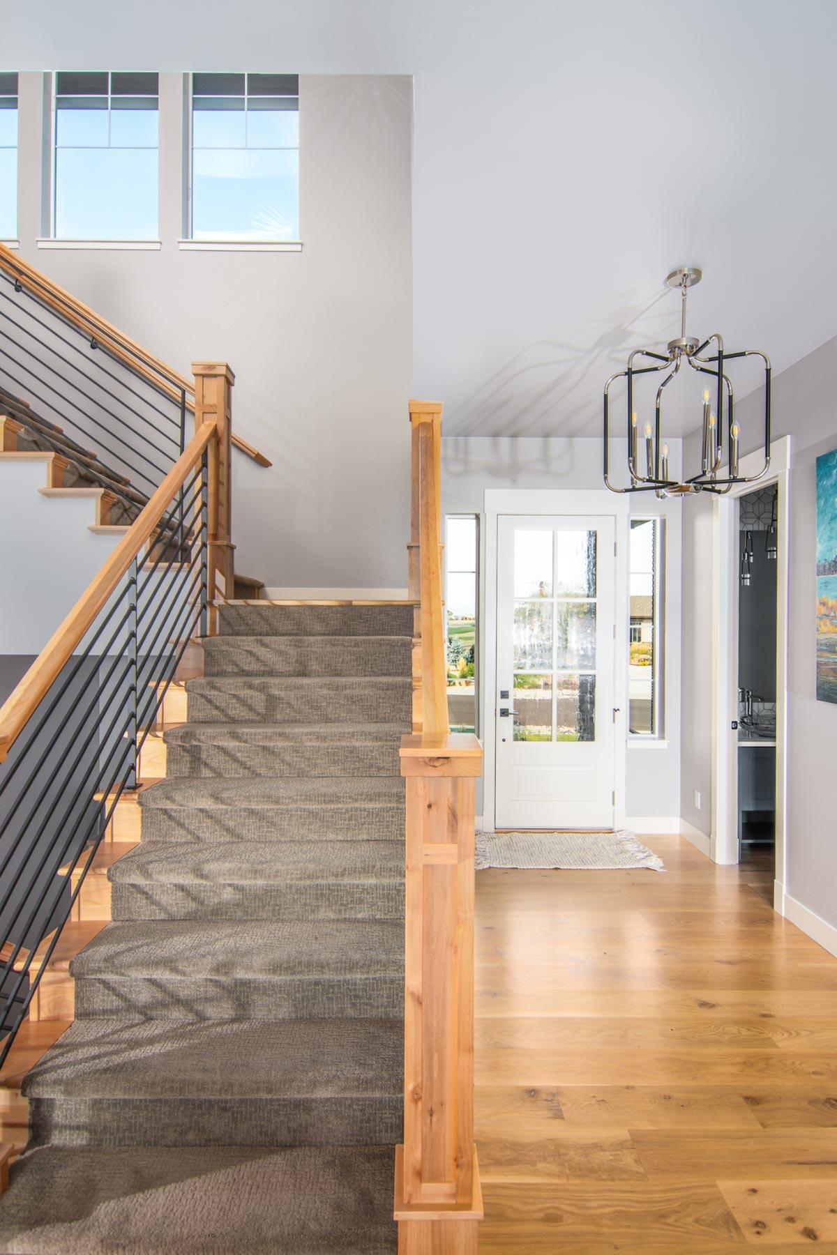 Interior view of a house entryway with carpeted stairs, wood flooring, a glass-paneled door, and a modern chandelier.