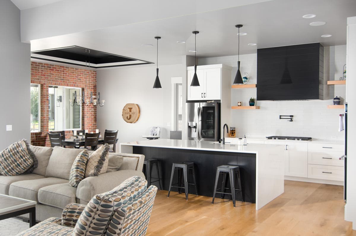 Open concept living area with brick accent wall, sectional sofa, and modern kitchen featuring a large island and black range hood.