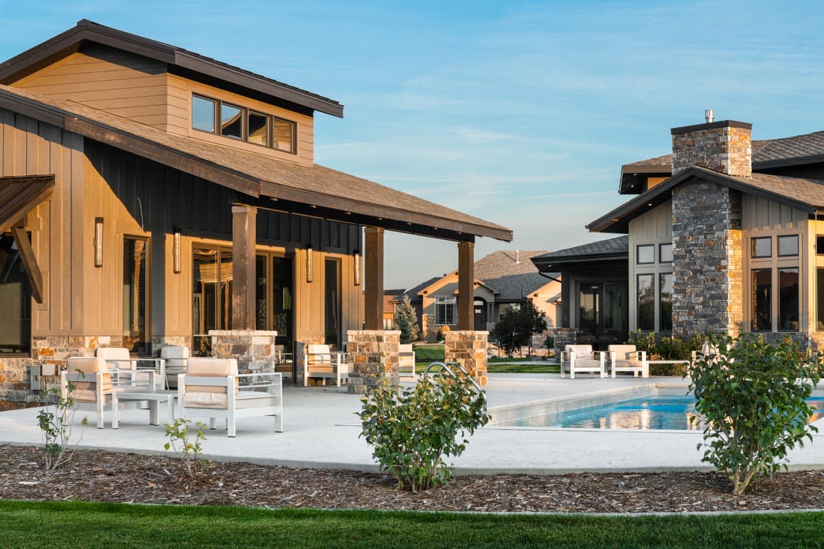 Modern house exterior with wood siding, stone accents, gabled roof, covered porch, and swimming pool.