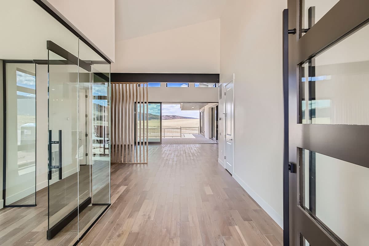 Interior view of modern house entry with glass walls, slatted wood screen, and expansive sliding doors to outdoor deck.