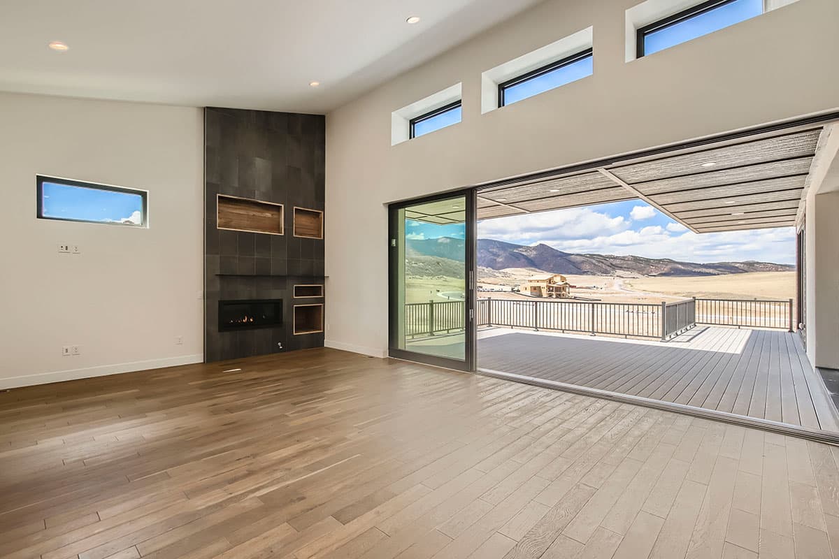 Living room interior with vaulted ceiling, fireplace, and large sliding glass doors opening to a deck with mountain views.