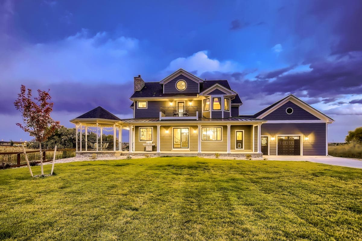 House plan exterior with wrap-around porch, bay window, second-story balcony, and attached garage.