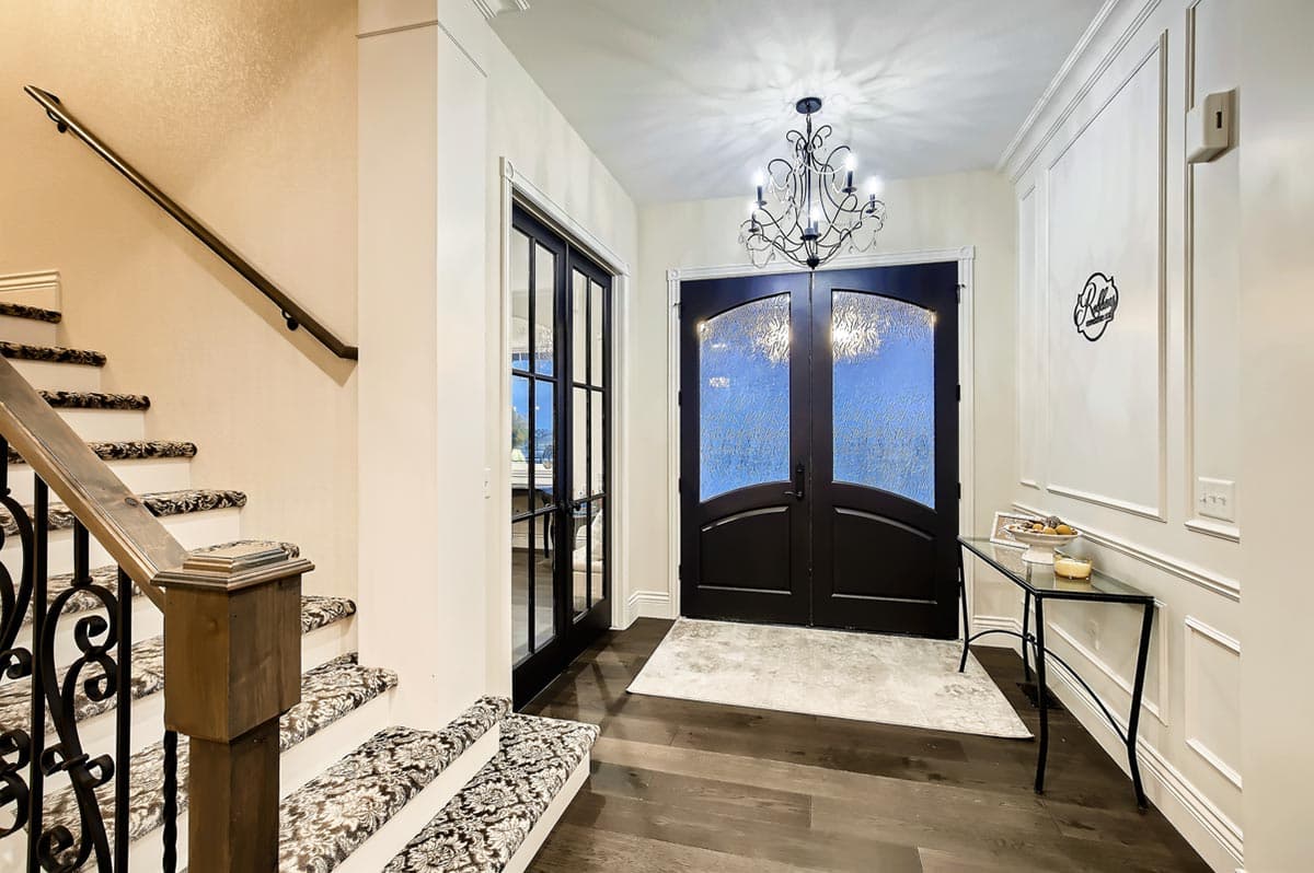 Foyer interior with double arched glass doors, carpeted stairs with ornate metal railing, and wainscoting.