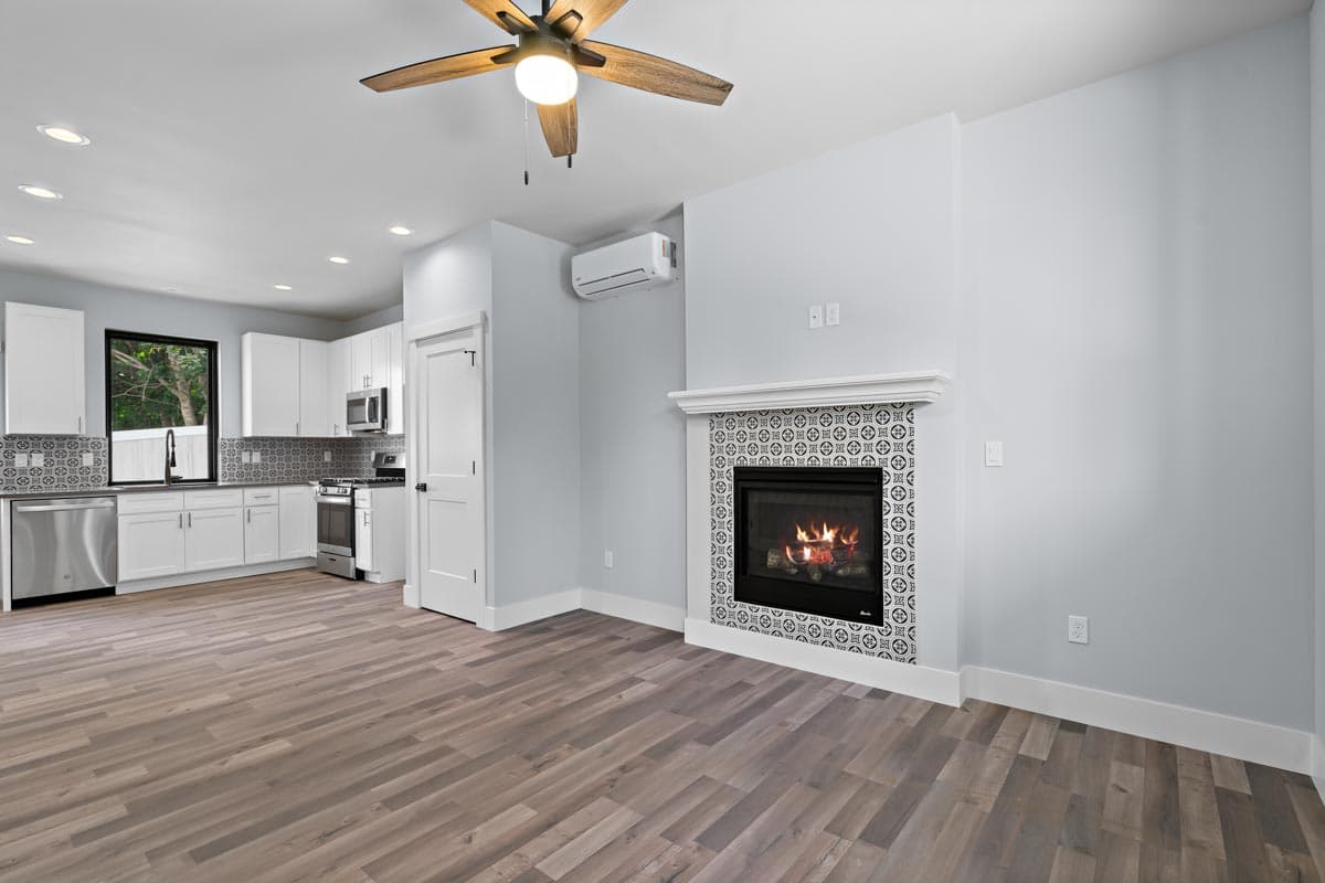 Open-plan living area with a modern kitchen featuring white cabinetry and a decorative tile backsplash next to a fireplace with similar tile surround.