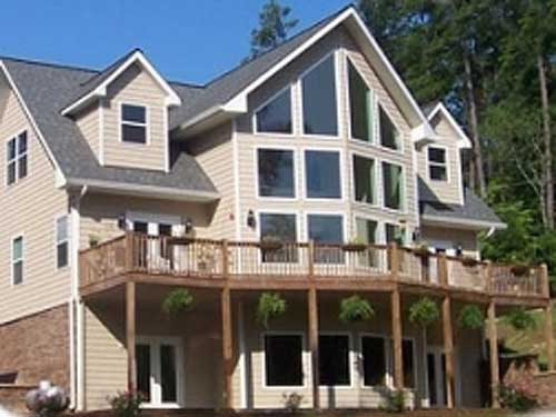 House plan exterior: Tall, multi-story home with a large, multi-pane window wall, wrap-around deck, and gabled dormers.