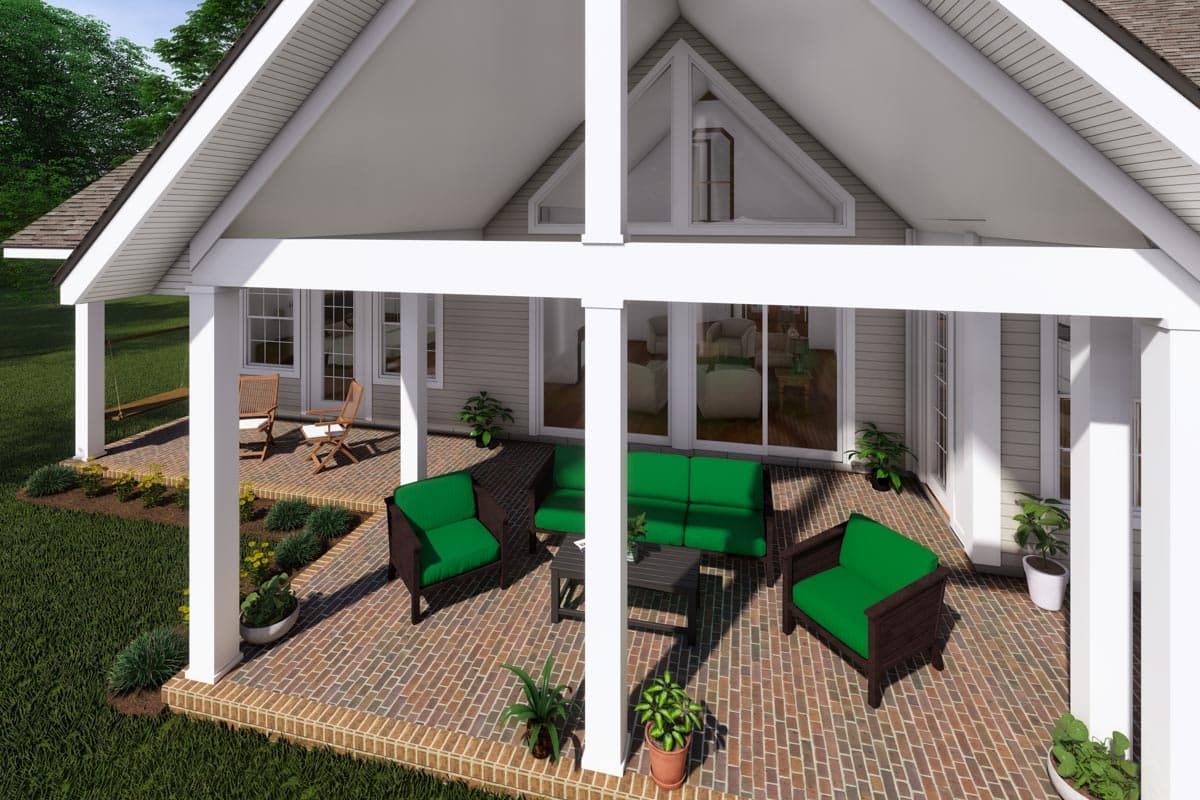 House plan exterior with gabled roof, wide porch, and multiple windows. Shows seating on brick patio.