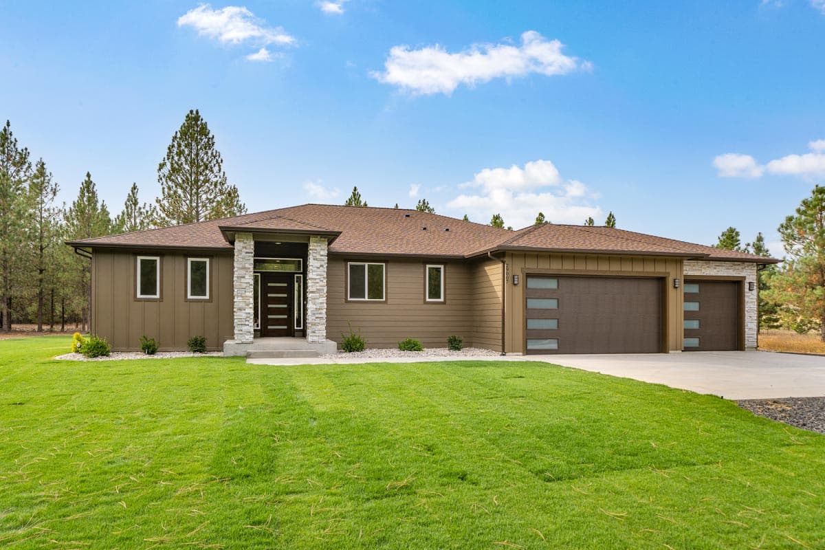 House plan exterior. Modern, one-story home with a flat roofline. Features include a covered entry, stone columns, and an attached garage.