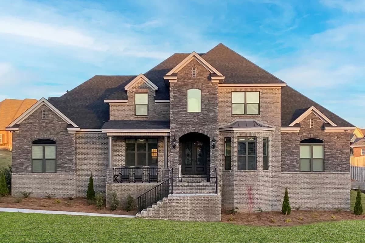 House plan exterior. Two-story home with brick and stone facade. Features include a front porch, gables, and a bay window.