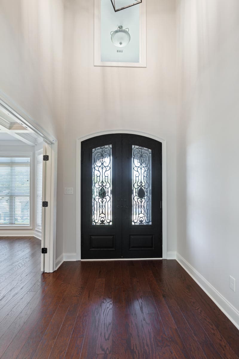 Foyer with arched double doors featuring decorative glass panels and a high ceiling with a chandelier.