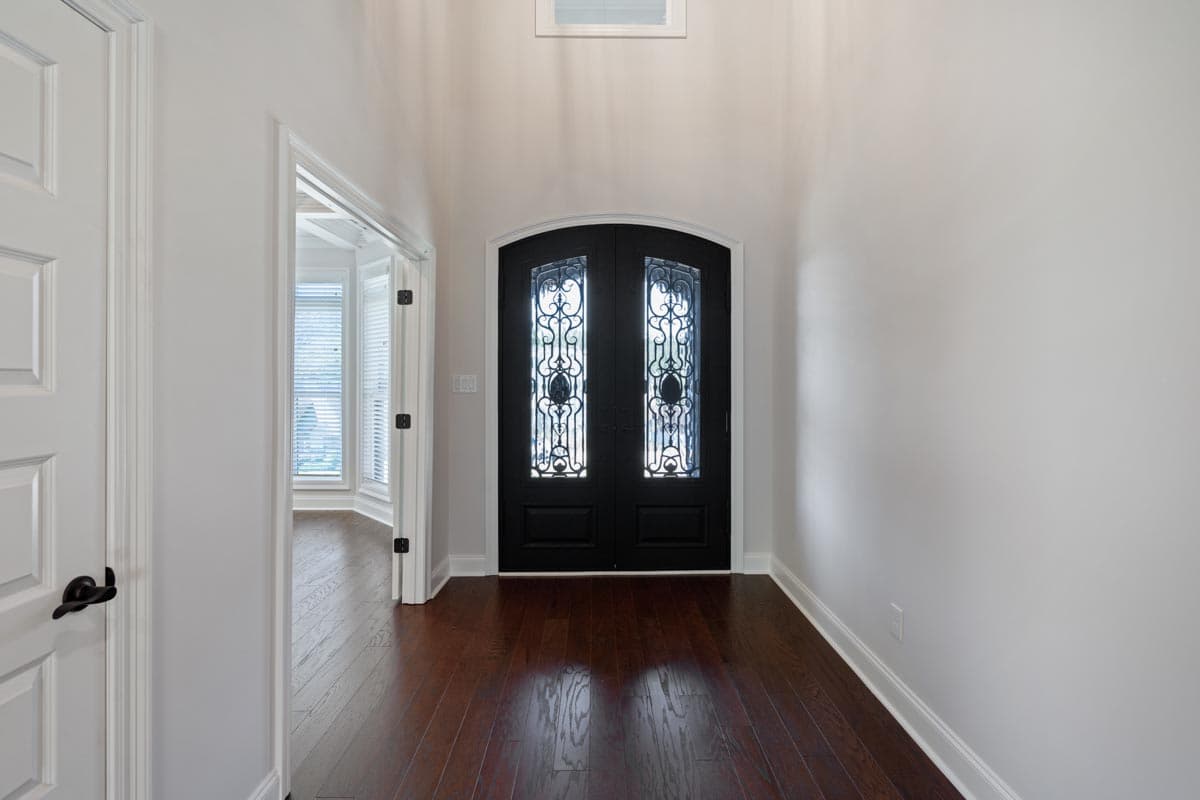Interior view of a grand entryway with black double doors featuring decorative glass, leading to a room with bay windows.