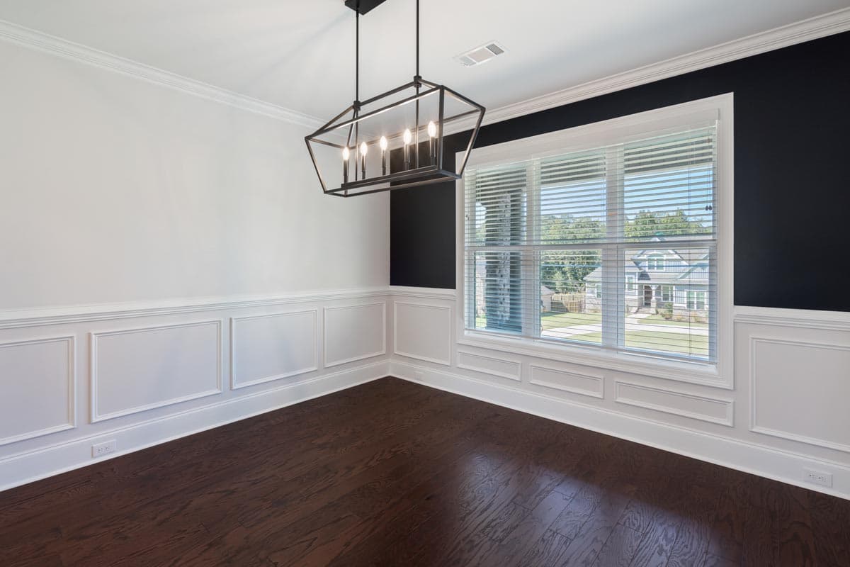 Interior view of a dining room with white wainscoting, dark hardwood floors, a large window, and a geometric pendant light.