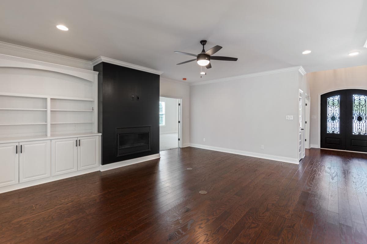 Interior view: Living room with built-in white shelving, black fireplace surround, ceiling fan, and arched double entry doors.