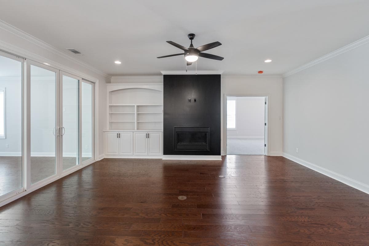Living room with dark hardwood floors, built-in white cabinetry, and a modern black fireplace with a ceiling fan.