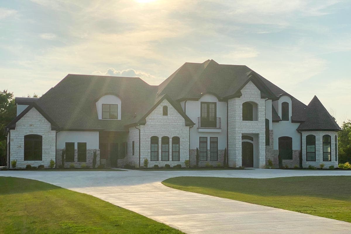 House plan exterior: large two-story residence with stone accents, multiple gables, arched windows, and a Juliette balcony.