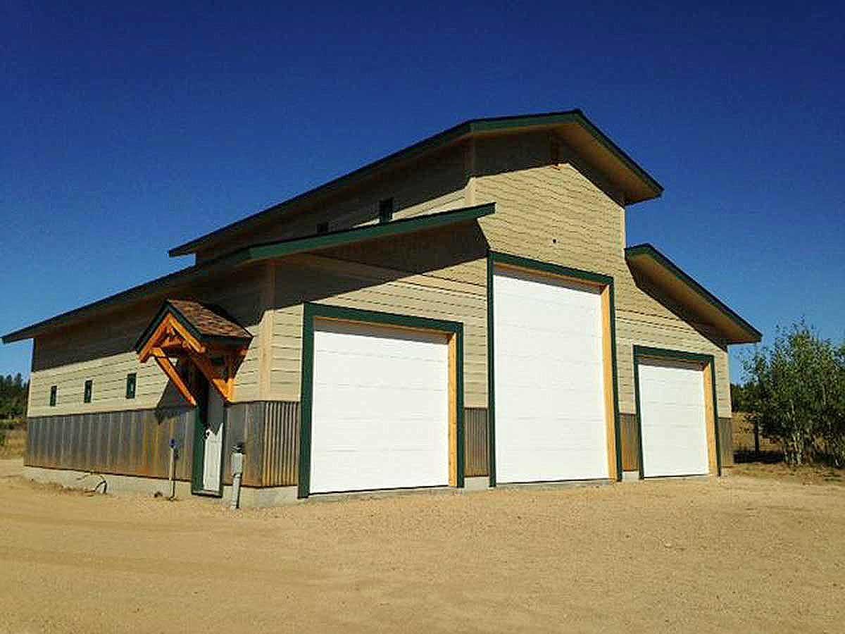 Exterior house plan with a tan siding, corrugated metal base, pitched roof, and three garage doors.