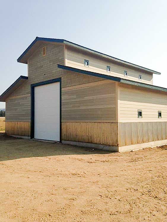 Barn-style building exterior with horizontal siding, a large overhead door, and multiple small dormer windows along the roofline.