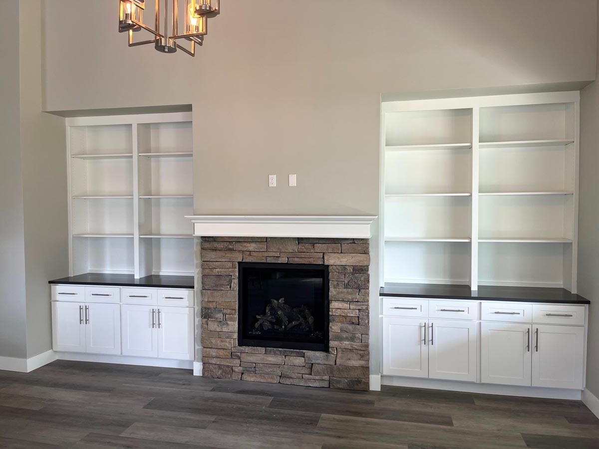 Interior view of a great room with a stone fireplace, built-in white cabinets, and open shelving flanking the fireplace.