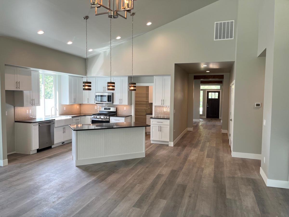 Open-concept kitchen with white cabinetry, island, and vaulted ceiling. Hallway leads to front door.