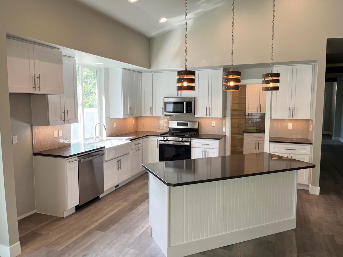 Kitchen with white shaker cabinets, farmhouse sink, dark countertops, island, and pendant lighting.