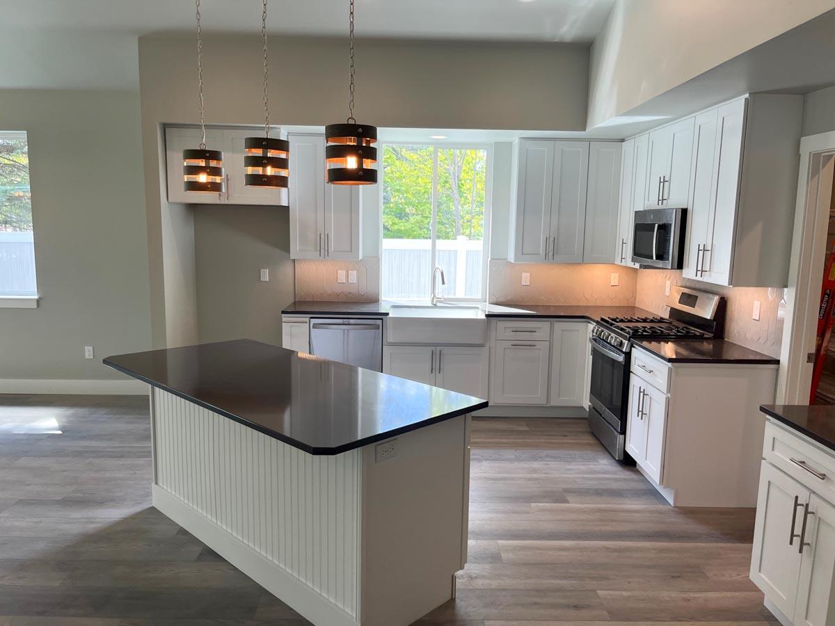 Kitchen with white cabinets, dark countertops, island, stainless steel appliances, and pendant lighting.