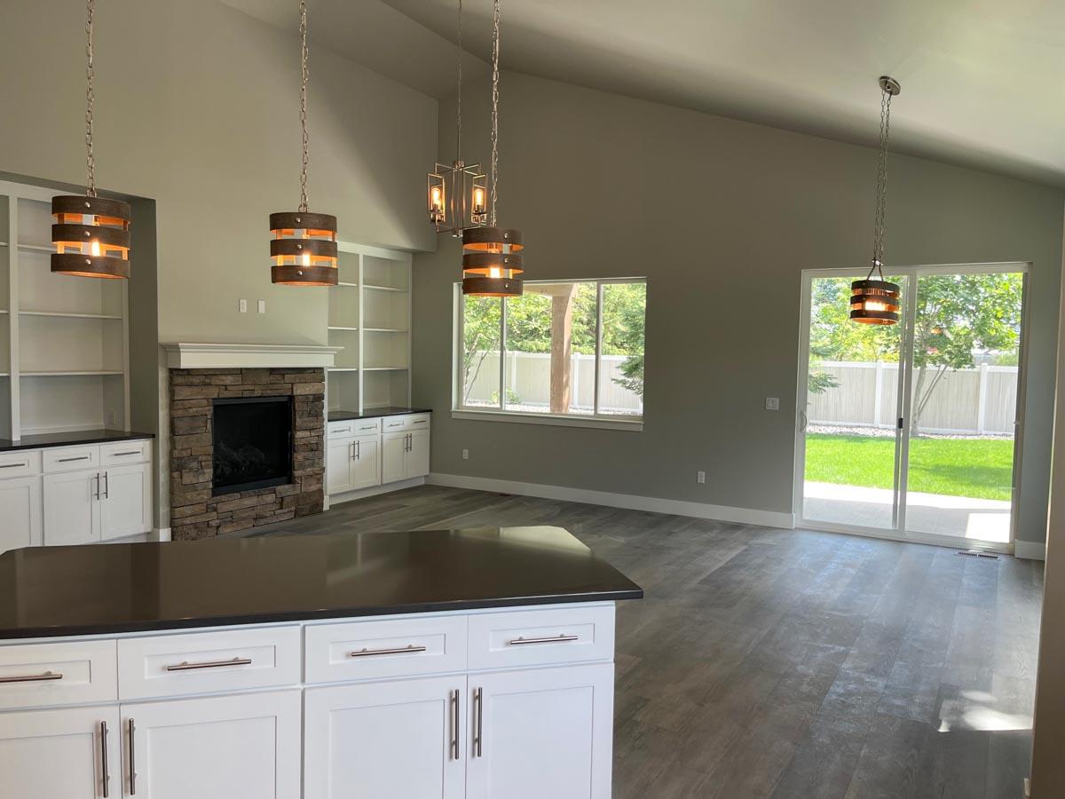 Open-concept living area with vaulted ceiling, stone fireplace, built-in shelving, and sliding glass doors to backyard.