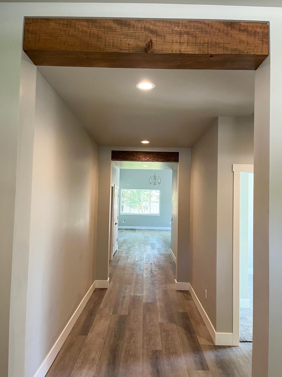 Hallway with wood beam accents, recessed lighting, and wood plank flooring leading to a room with large windows.