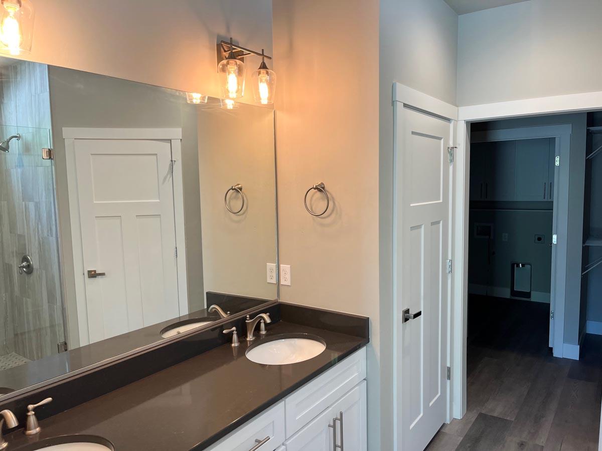 Bathroom with double vanity, modern lighting, glass-enclosed shower, and doorway to laundry area.