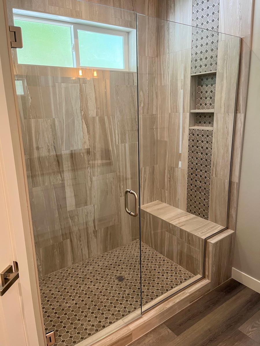 Enclosed glass shower with large format tile walls, mosaic tile accents, built-in bench, and hexagonal tile floor.
