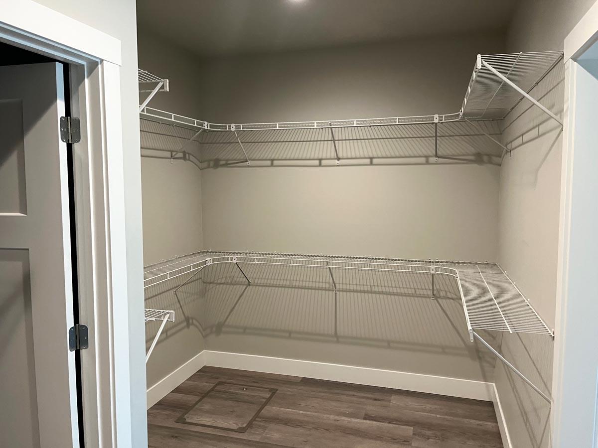 Walk-in closet with L-shaped shelving on two walls, recessed lighting, and dark wood laminate flooring.