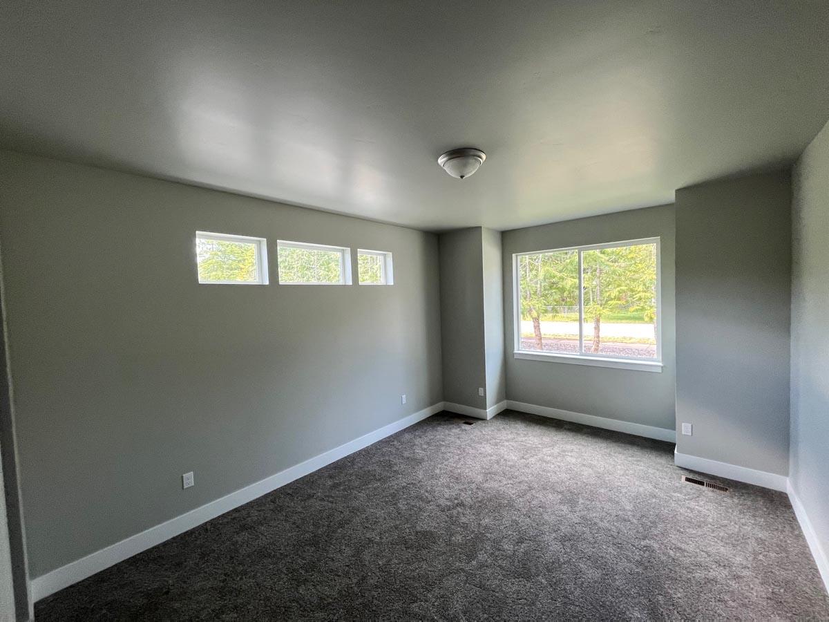Interior view of an empty room with carpet, a large picture window, and a row of three horizontal windows.