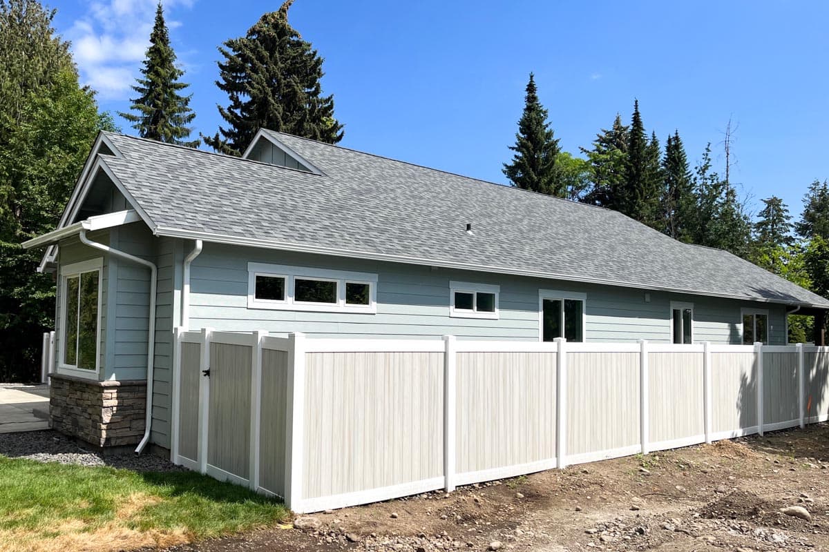 Modern ranch house plan exterior with horizontal siding, gabled roof, stone foundation, and vinyl privacy fence.