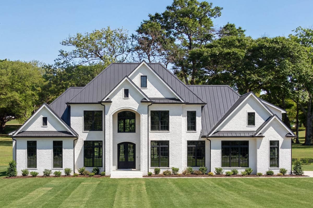 House plan exterior with white brick facade, dark metal roof, and multiple gables. Features a two-story design and large windows.