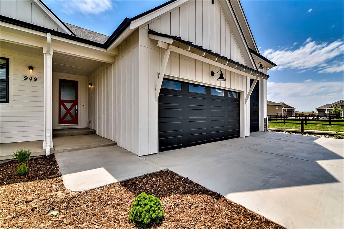 Modern Farmhouse house plan exterior with white vertical siding, covered porch, red door, and two-car garage with black doors.
