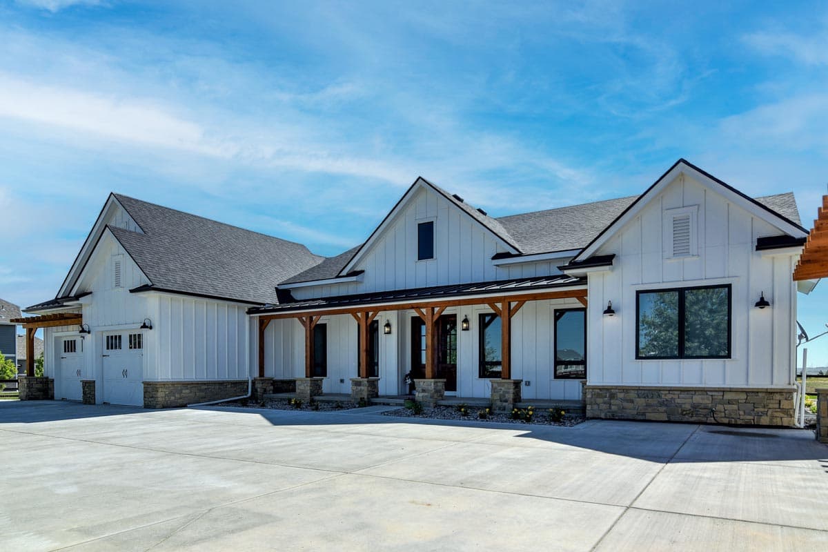 House plan exterior. Modern Farmhouse style with a single story, multiple gables, a covered porch, and a detached garage with pergola.