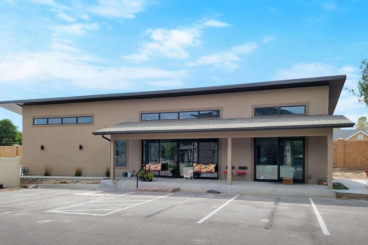 Modern house plan exterior with a flat roof, stucco finish, and a covered porch with large glass doors.