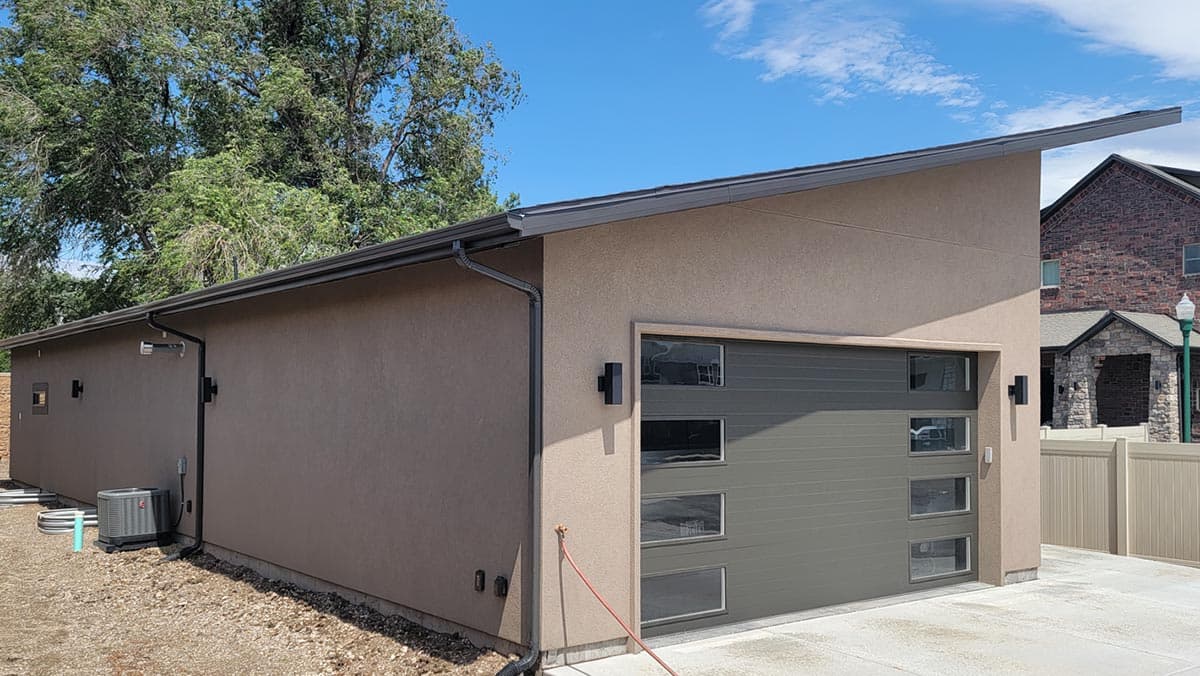Modern house plan exterior with stucco finish, asymmetrical roofline, and a segmented garage door with horizontal windows.