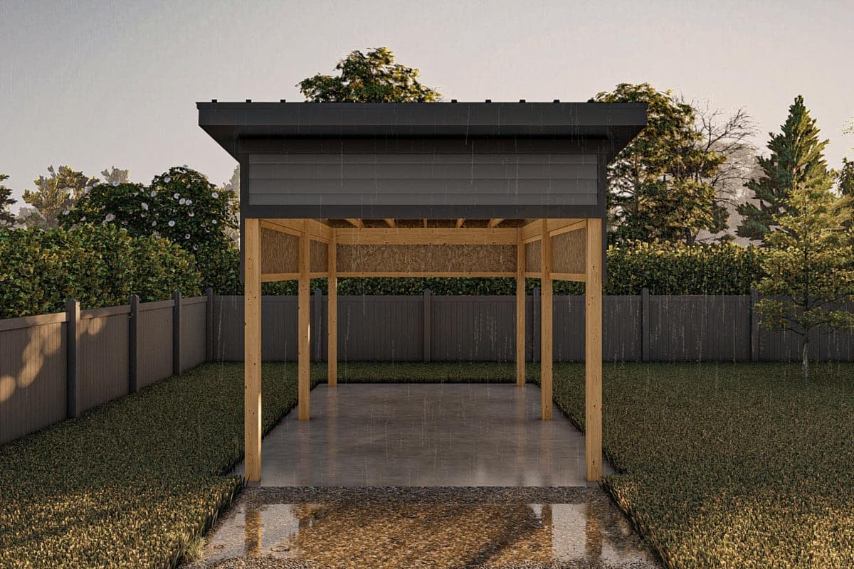 Open-air pavilion with wooden posts, concrete floor, and dark sloped roof, set in a backyard during rain.