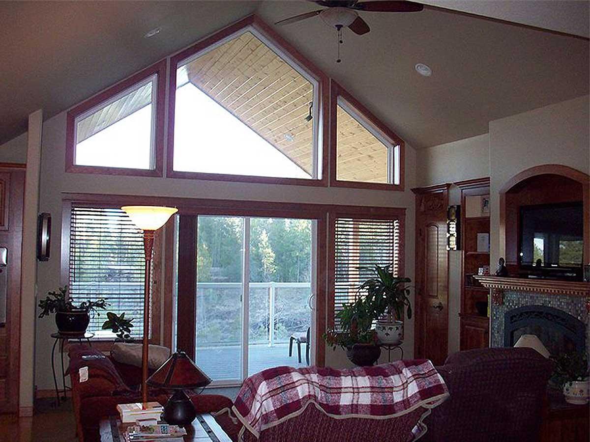 Interior view of a great room featuring a vaulted ceiling, large triangular windows, a fireplace, and a sliding glass door.