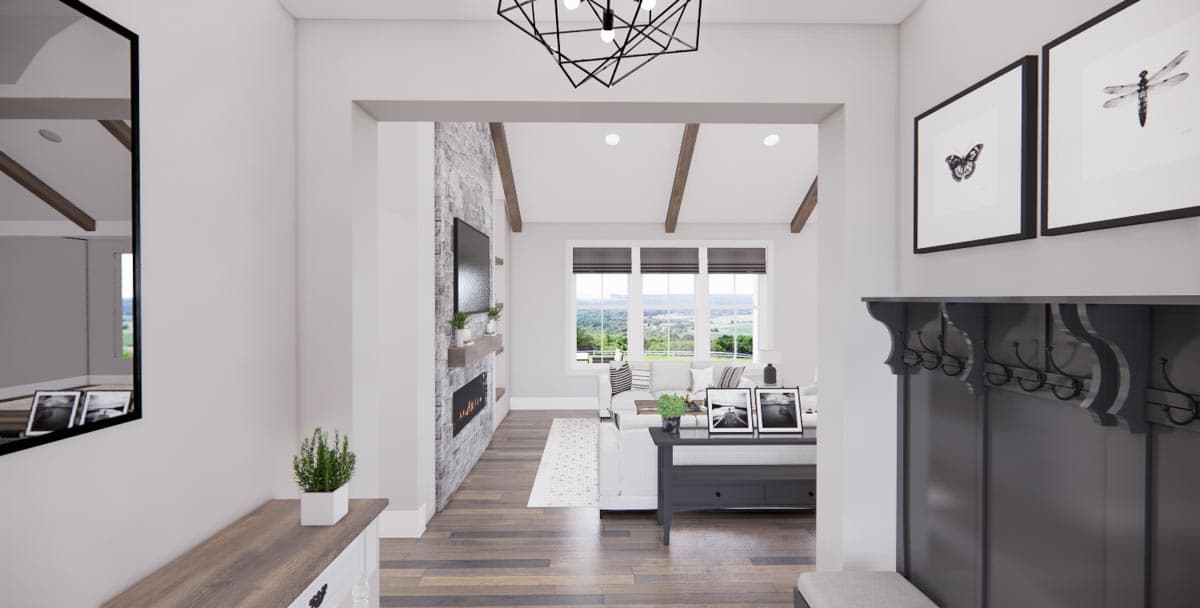 Interior view of a great room with stone fireplace, vaulted ceiling with beams, and large windows overlooking a landscape.