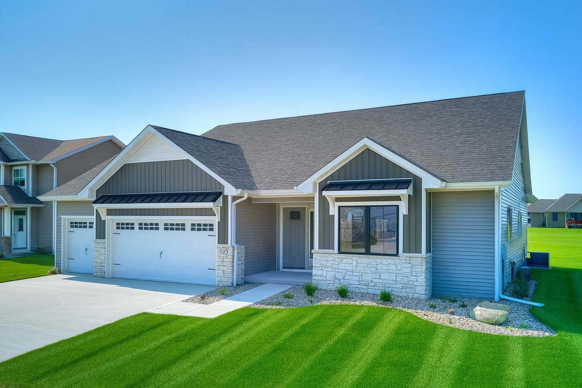 Modern ranch house plan exterior with attached three-car garage, gabled dormers, and stone accent skirting.