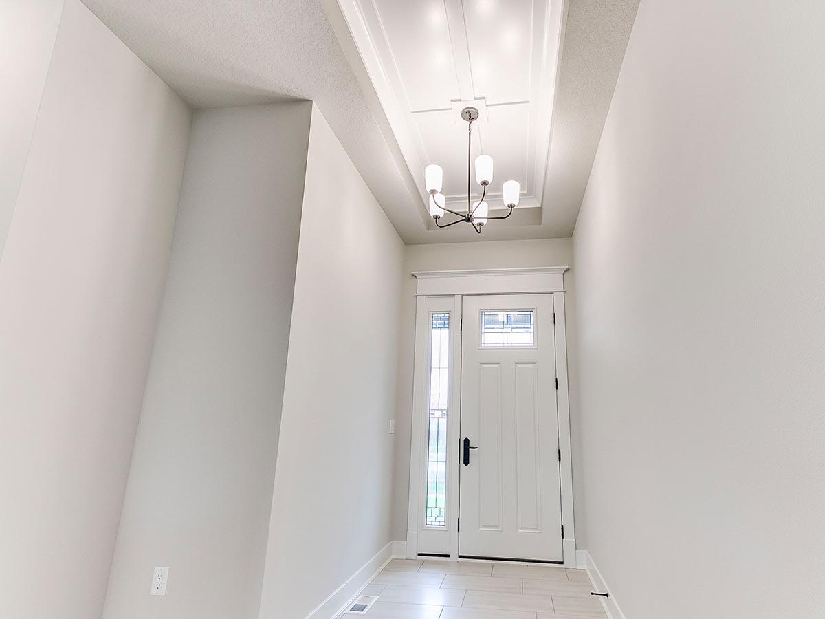 Interior view of a house foyer with a white front door, sidelight windows, and a coffered ceiling with chandelier.