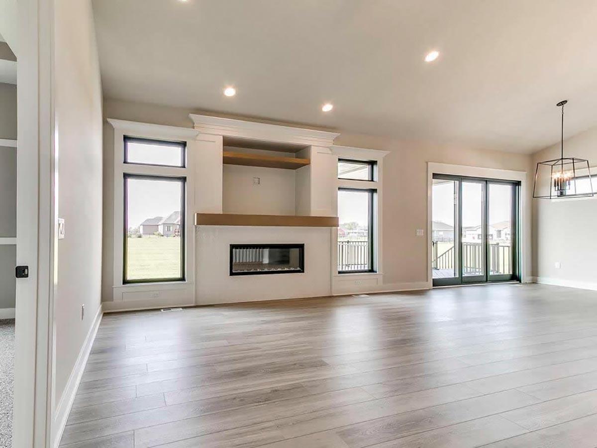 Great room with modern fireplace, large windows, sliding glass doors, and wood plank flooring.