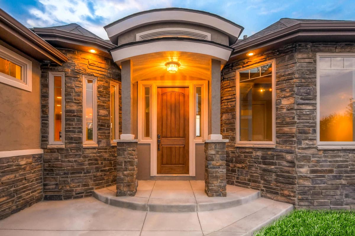 House plan exterior with stone facade, arched entryway, wood door, and multiple windows.